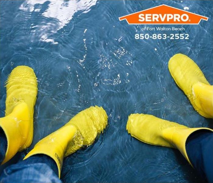 People in yellow rubber boots stand in water covering a floor.