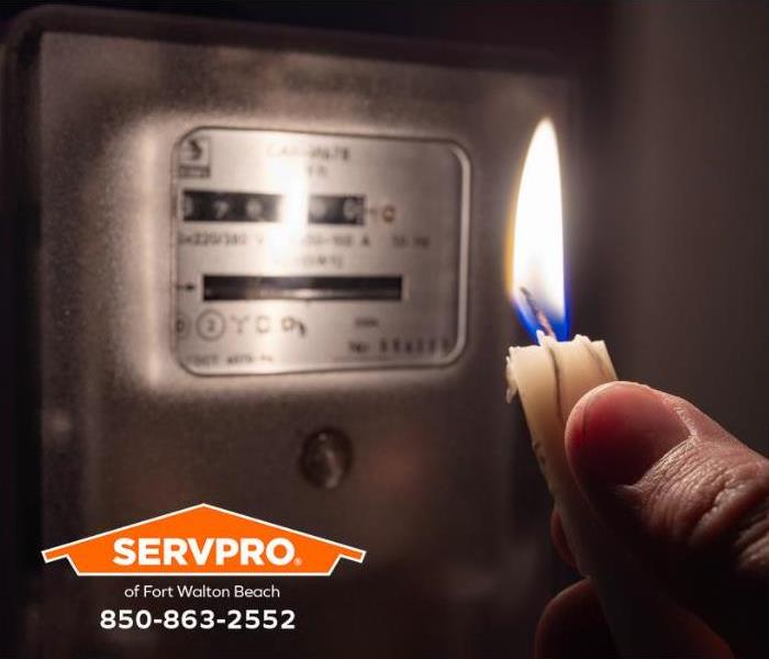 A person holds up a candle to read an electric meter at home.